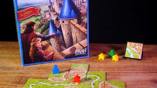 Carcassonne box, meeple, and tiles laid out on a wooden table